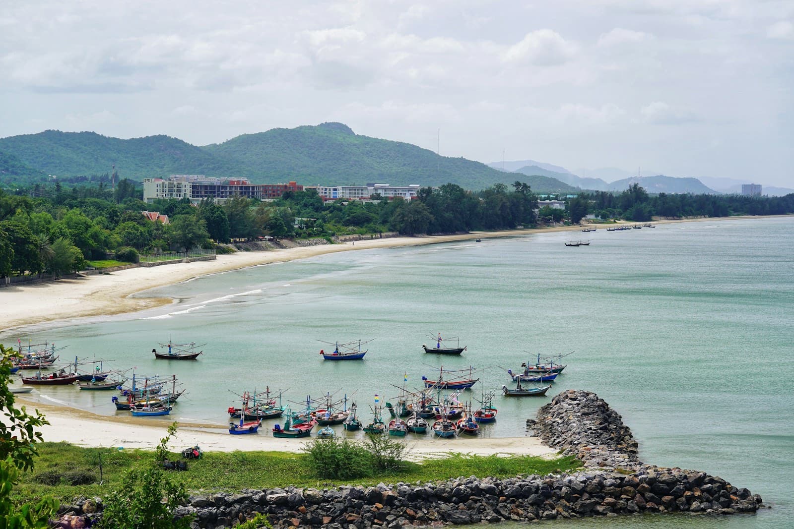 เรือประมงจอดในอ่าวสงบที่หาดเขาเต่า หัวหิน มีเนินเขาเขียวอยู่ด้านหลัง